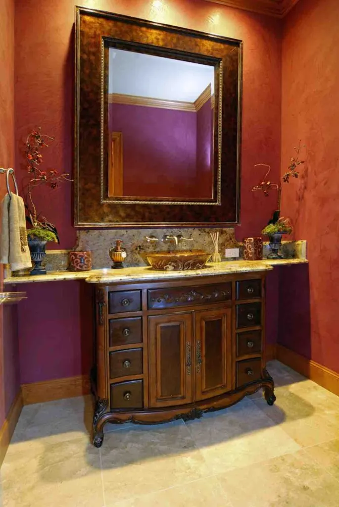 22 Inspiring Bathroom Paint Colors 15 A compact powder room with large framed mirror, ornate vanity, and dark red painted walls.