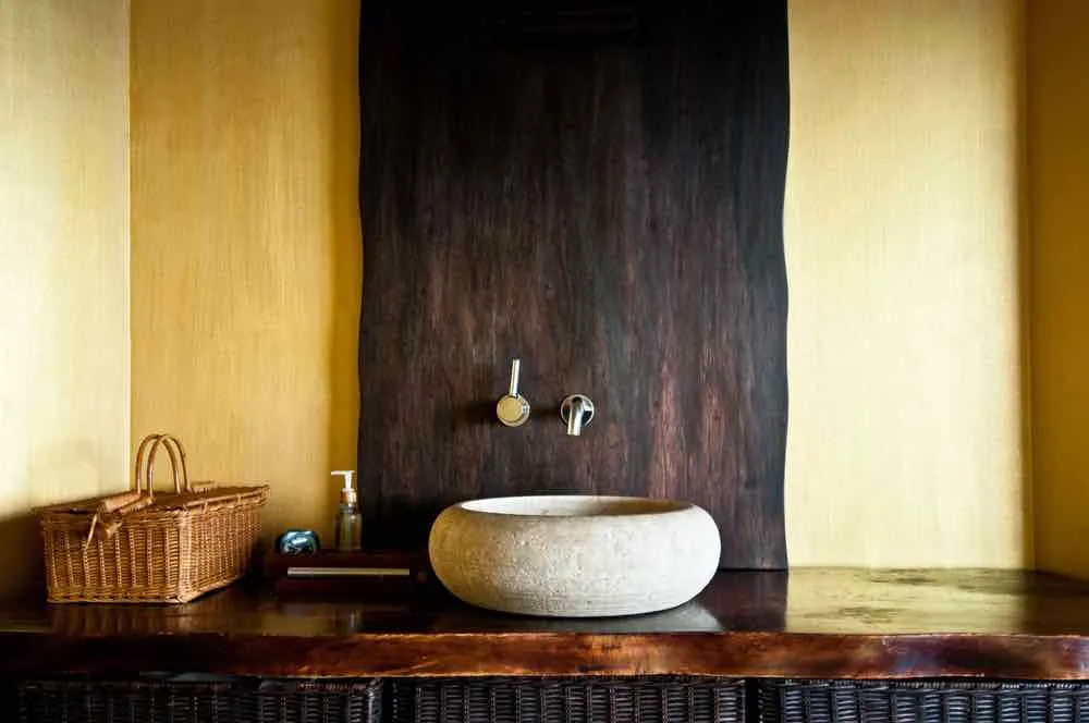 22 Inspiring Bathroom Paint Colors 8 A bathroom vanity with muted yellow paint, stone sink, and dark wood countertop.