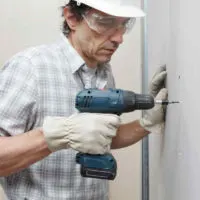 man using a cordless drill to hang drywall