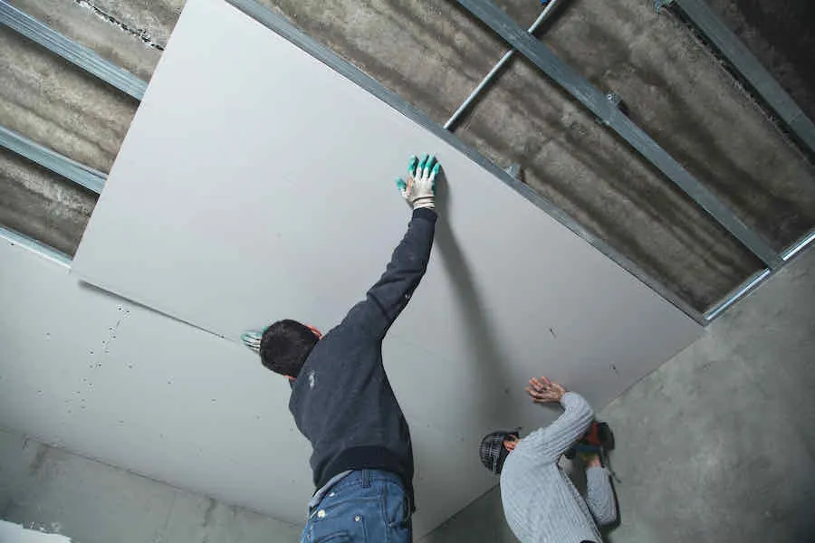 How Much Does It Cost to Install Drywall? 3 workers hanging drywall panel on ceiling