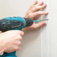 person fastens drywall nails with a screwdriver