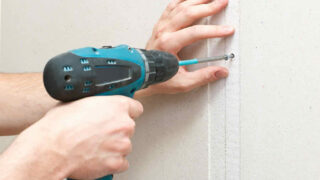 person fastens drywall nails with a screwdriver