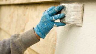 A painter applying the best exterior primer to a wooden home exterior