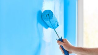 Man rolling blue paint onto a wall.