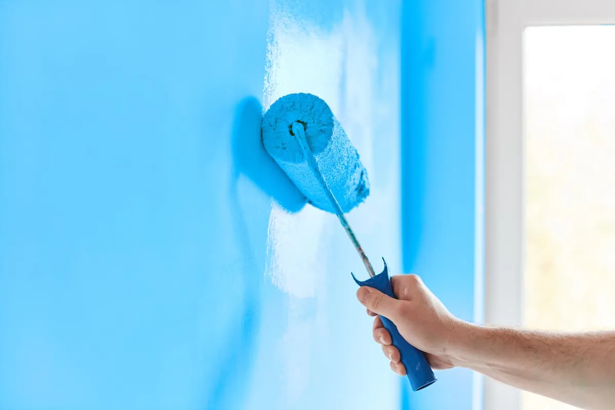 Man rolling blue paint onto a wall.