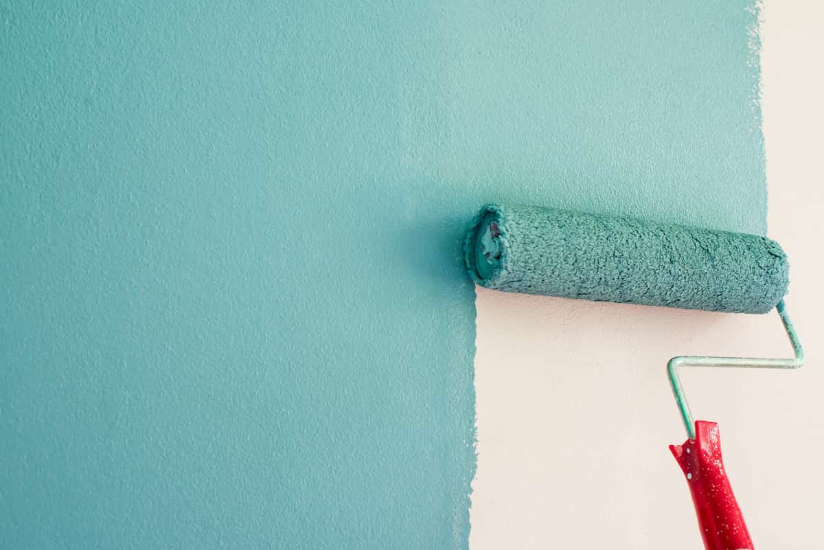 Using a paint roller to paint a wall teal.