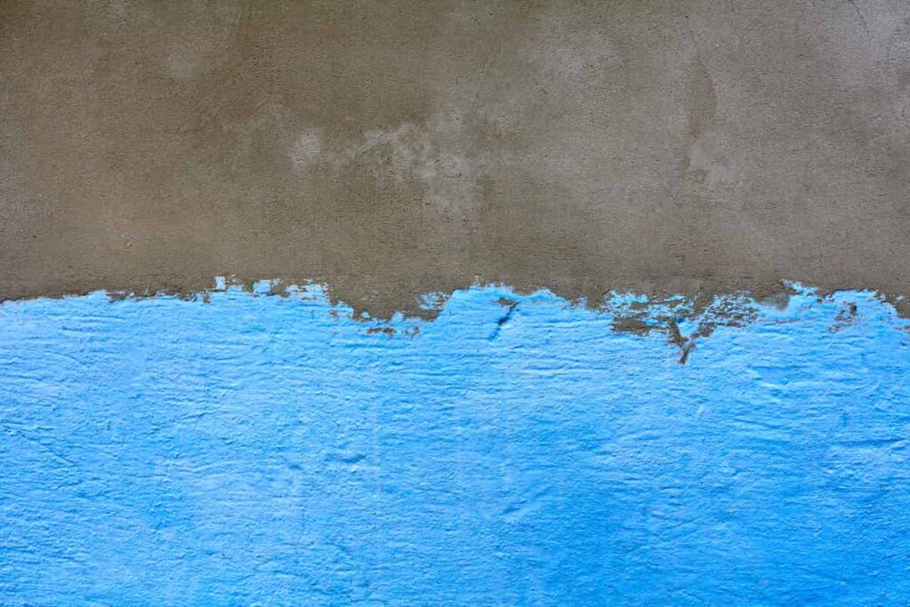 A concrete wall partially painted sky blue paint.