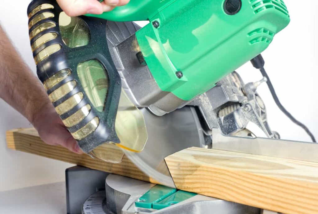 24 DIY Home Improvement Tools Every Homeowner Should Have 4 Person using a green compound miter saw to cut lumber.