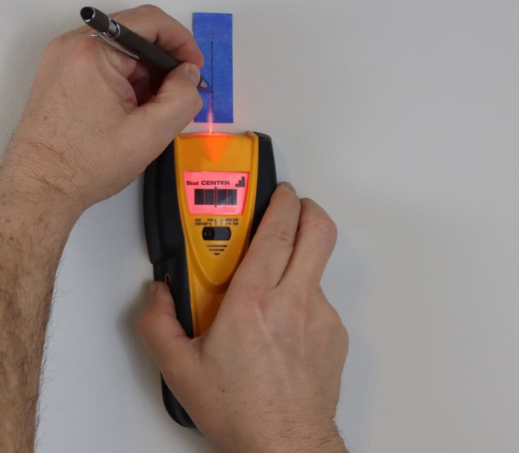 24 DIY Home Improvement Tools Every Homeowner Should Have 2 Man using a stud detector and marking the location on a piece of blue masking tape.