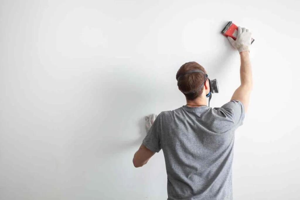 How to Repair Drywall: From Holes to Perfect Walls 5 A man wearing a respirator while sanding drywall