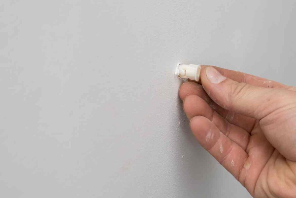 A man's hand showing how to remove drywall anchors
