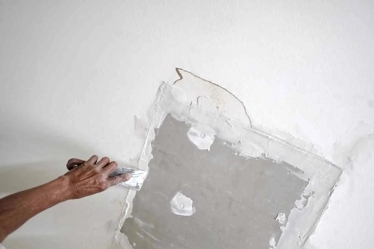 Man's hand with a putty knife showing how to repair drywall damage