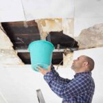 Man holding a bucket up to catch water while thinking about drywall repair cost