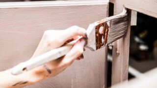 Close up of a person holding a paintbrush painting kitchen cabinets without sanding