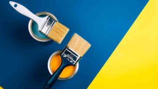 Two open cans of paint with paintbrushes and blue and yellow background. Behr Dynasty vs Marquee