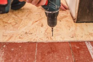 Person using a drill to install screws when replacing bathroom subfloor