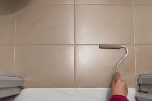 A person painting bathroom tile with a foam roller
