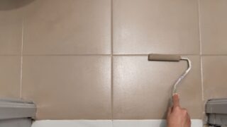 A person painting bathroom tile with a foam roller