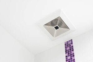 Bathroom fan in a ceiling with a strip of purple tile.